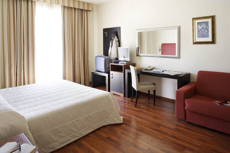 Camera semplice e luminosa con parquet, scrivania e divano. Spazio accogliente e funzionale per relax e lavoro.