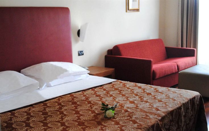 Camera di hotel con arredamento semplice, dotata di letto matrimoniale e un divano, ideale per un soggiorno confortevole.