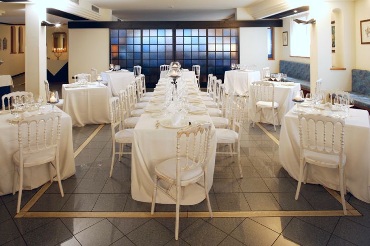 Spazio dedicato alla ristorazione, con tavoli decorati in bianco e sedie abbinate. L'ambientazione è sobria e accogliente, adatta per eventi.