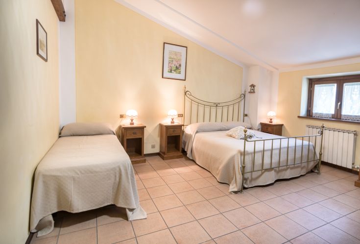 Camera semplice e confortevole con letti singoli e matrimoniali, illuminata da lampade funzionali.