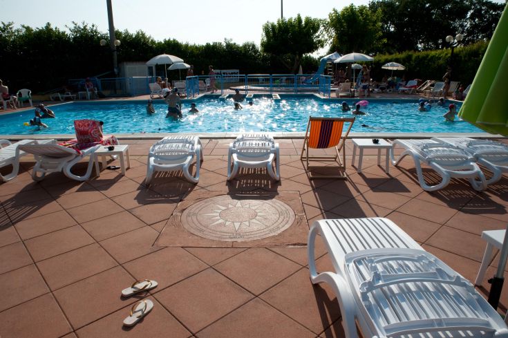 Una giornata estiva in piscina, con lettini a disposizione e diverse persone che si godono il bagno.