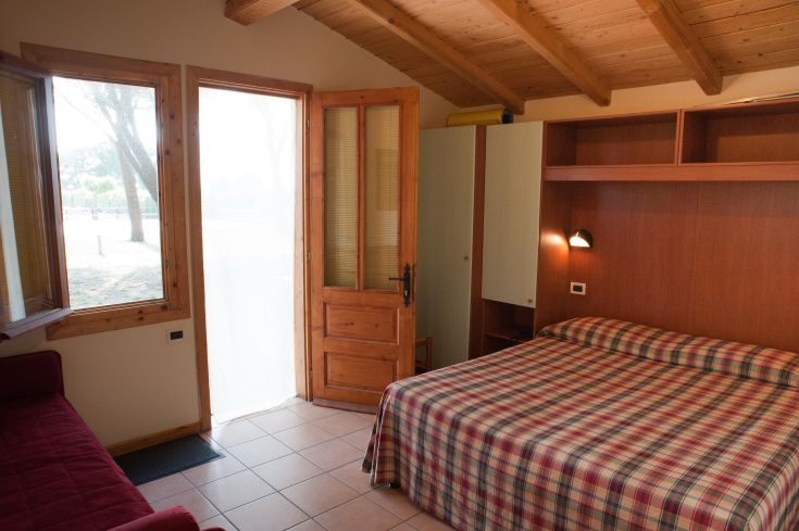 Camera semplice e luminosa in un villaggio turistico circondato da alberi. Ideale per famiglie e momenti di relax.