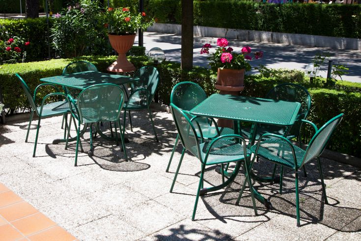 Outdoor area with green tables and chairs surrounded by blooming flowers and lush vegetation.
