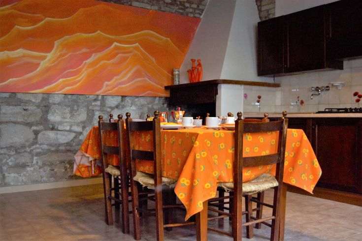 Eine Esszimmer-Szene mit einem Tisch, der mit einem orangefarbenen Tischdecke in einer rustikalen, gemütlichen Umgebung gedeckt ist.