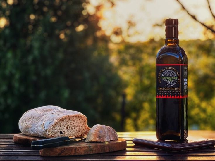 Olivenöl und frisches Brot auf einem Tisch, umgeben von Grünanlage.