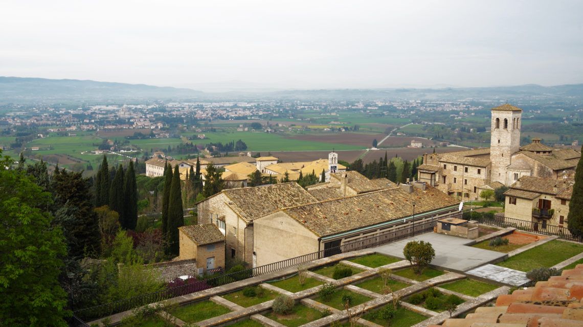 Panorama von Assisi, das historische Gebäude und grüne Hügel im Hintergrund zeigt.