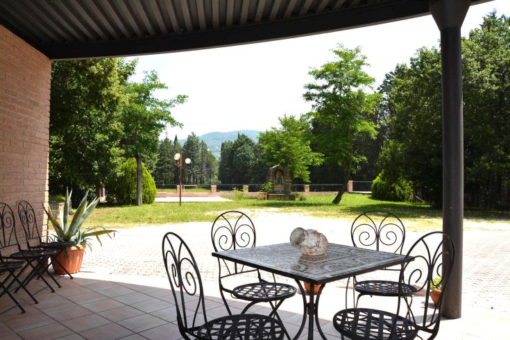 Eine Außenterrasse mit Tisch und Stühlen, umgeben von Grünflächen und Pflanzen.