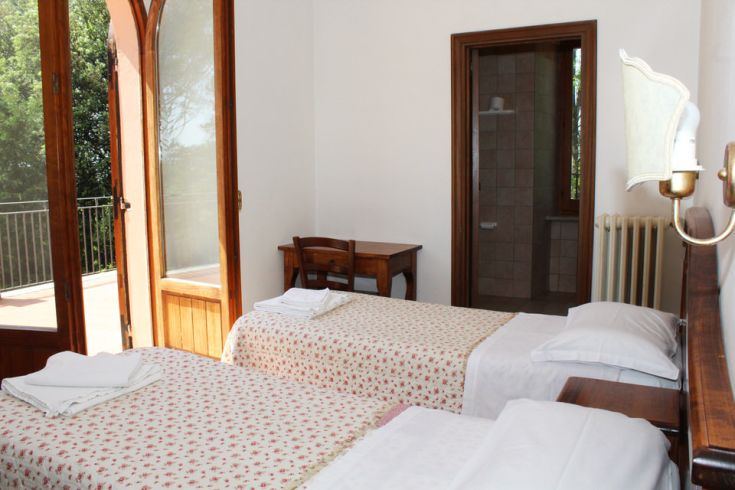 Einfaches Zimmer mit Einzelbetten, natürlich beleuchtet und mit Blick auf ein grünes Gebiet.