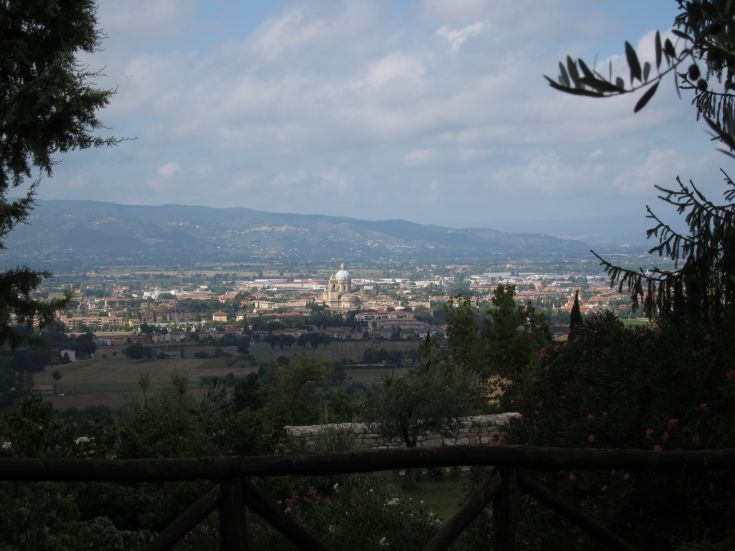 Panorama di Assisi con colline circostanti e un monastero circondato dalla vegetazione.