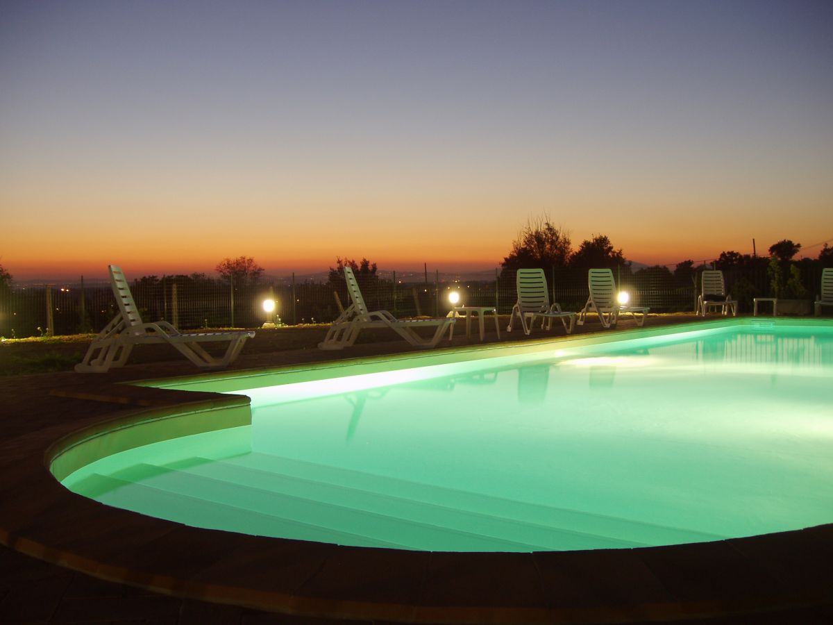 Evening view of a lit pool surrounded by lounge chairs and a gradient sky at sunset.