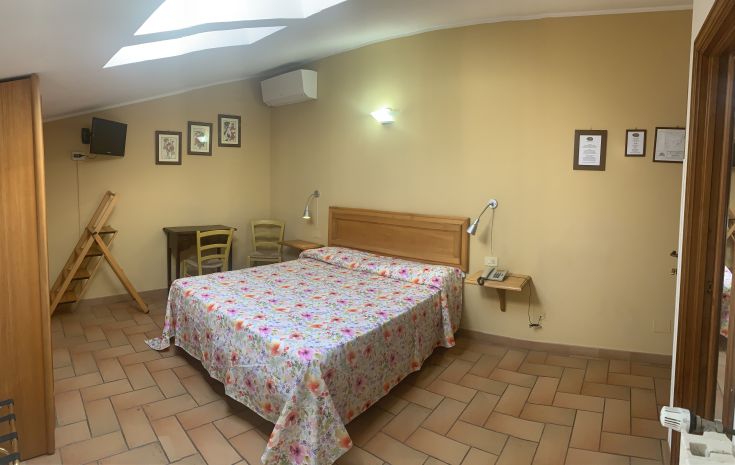 Einfache Zimmer mit einem Doppelbett, floralen Bettlaken, sauber und funktional mit Grundkomfort.