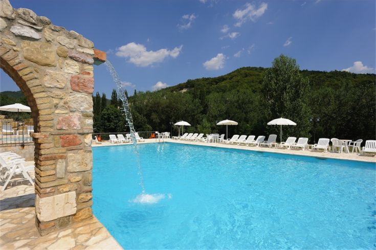 Une piscine naturelle entourée de verdure, équipée de parasols et de chaises longues pour se détendre.