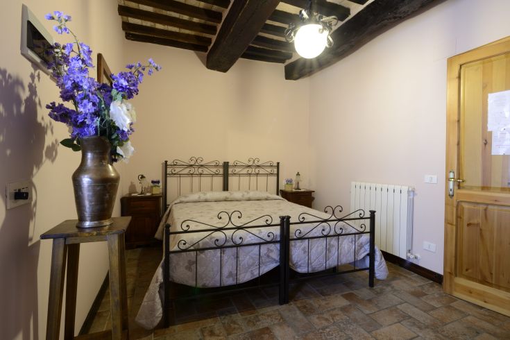 Chambre confortable avec un lit en fer, un sol en pierre et quelques décorations florales.