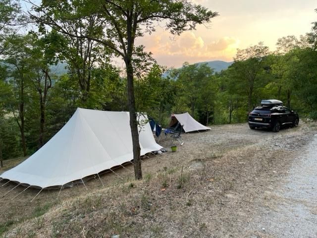 Une zone de camping paisible entourée d'arbres, avec des tentes et une voiture garée sous un ciel crépusculaire.