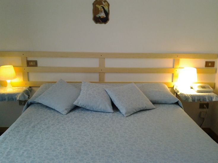 Simple hotel room with neatly made beds, warm lighting, and a religious painting on the wall.
