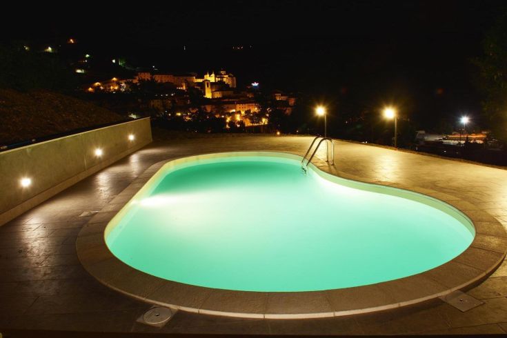 A night-lit swimming pool in a villa, offering a view of a serene landscape.