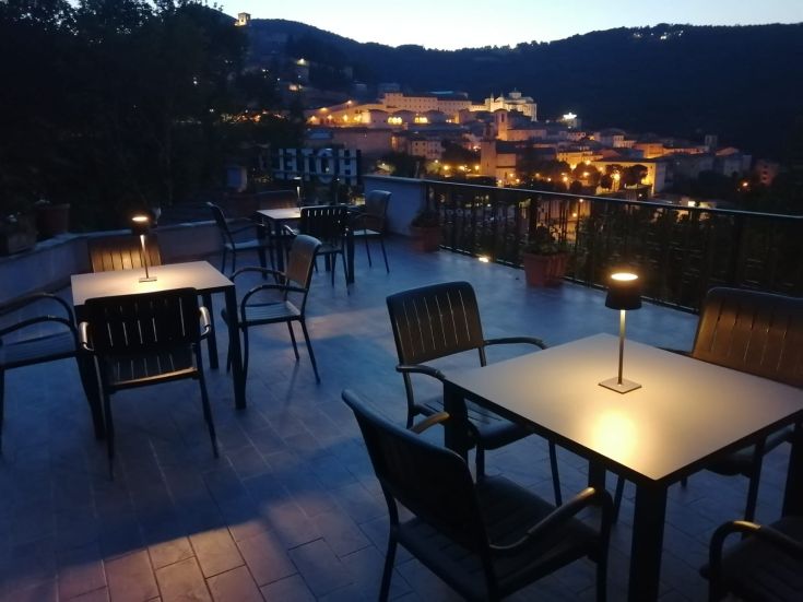 Hotel terrace with simple tables and a view of the brightly lit city at night.
