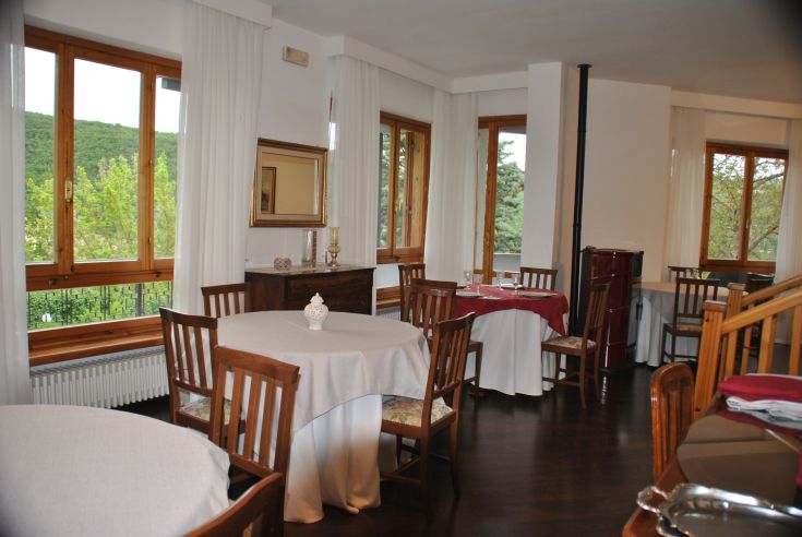 Restaurant with large windows overlooking greenery, simply and functionally furnished.