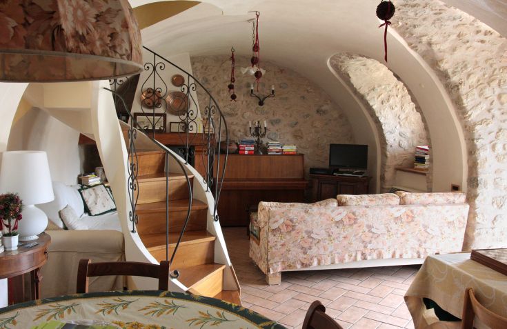 Salon informel avec des meubles rustiques, des murs en pierre et un escalier en colimaçon menant aux étages supérieurs.