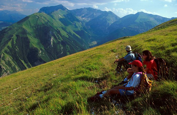 Des randonneurs se reposent sur une prairie verte, entourés de montagnes bien dessinées.