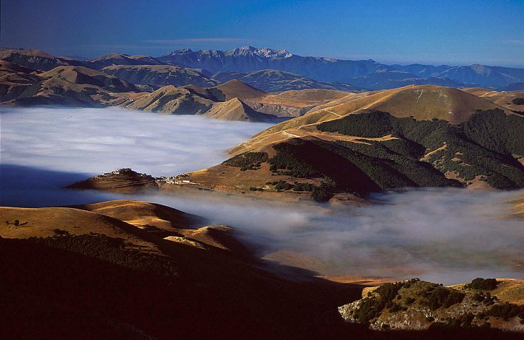 Vue panoramique dans le Parc National des Monts Sibillini avec des collines verdoyantes et des nuages dans le ciel.