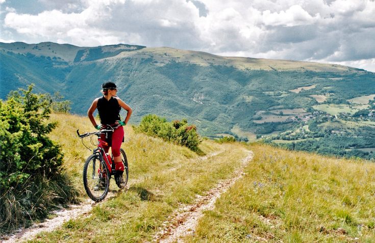 Une cycliste s'arrête pour admirer le panorama montagneux, immergée dans la nature environnante.