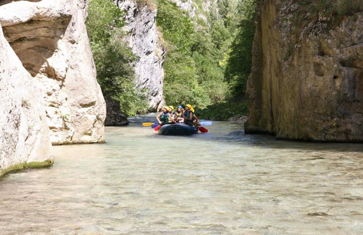 Un groupe de personnes fait du rafting entre des formations rocheuses et de la végétation verte.