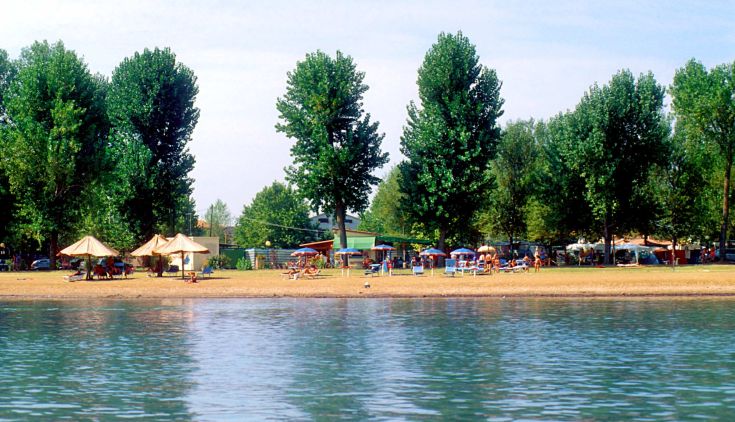 Une scène paisible de camping au lac Trasimeno, avec des espaces verts et des parasols pour l'ombre.