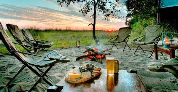 Zone de camping équipée de chaises et de feux de camp, immergée dans le calme du coucher de soleil.