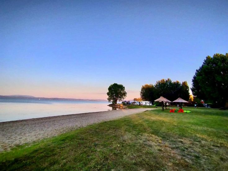 Une vue paisible du coucher de soleil sur le lac, entourée d'arbres et de parasols offrant de l'ombre.