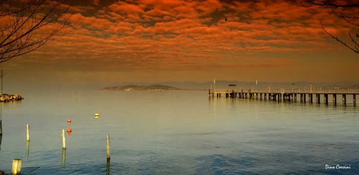 Coucher de soleil sur le lac Trasimène avec des nuages aux tons chauds au-dessus d'un quai tranquille.