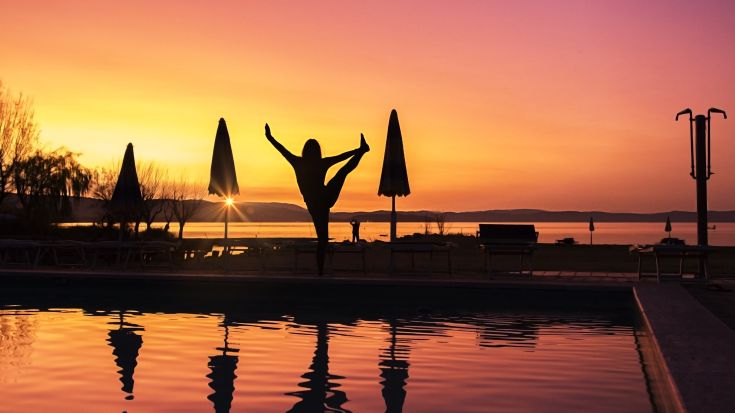 La silhouette di una persona si staglia al tramonto, riflessa nella piscina in un'atmosfera tranquilla.