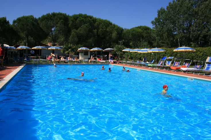 Una piscina blu all'interno del Badiaccia Camping Village, circondata da lettini e ombrelloni per rilassarsi.