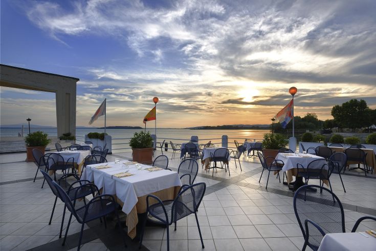 Un ristorante all'aperto con panorama sul Lago Trasimeno al tramonto, che offre un'atmosfera tranquilla.