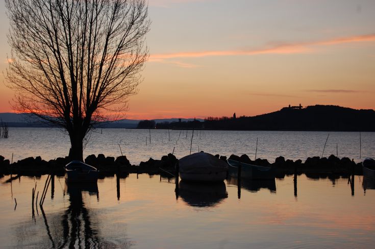 Tramonto sul Lago Trasimeno, con barche che galleggiano e riflessi sul'acqua serena.