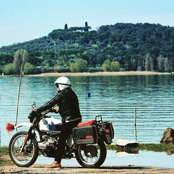 Un motociclista si trova nei pressi del Lago Trasimeno, in una giornata tranquilla e serena, immerso nel verde circostante.