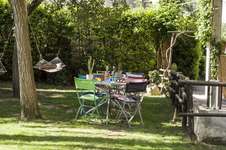 Ein gemütlicher Außenbereich mit einem bunten Tisch und Hängematten, umgeben von Grün.