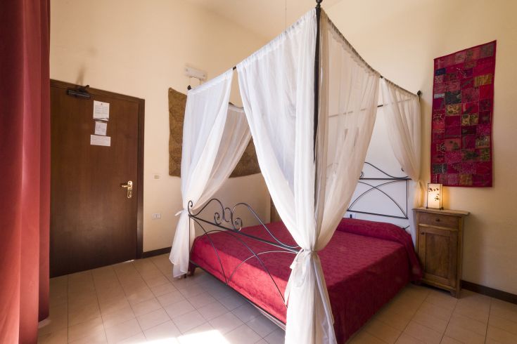 Ein einfaches Zimmer mit einem Himmelbett und einigen dekorativen Elementen.