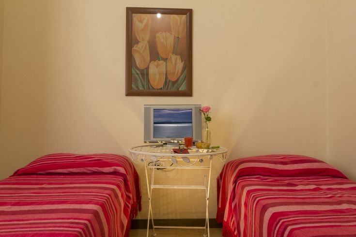 Einfache und gemütliche Zimmer mit gestreiften Betten und einem Fernseher zum Entspannen.