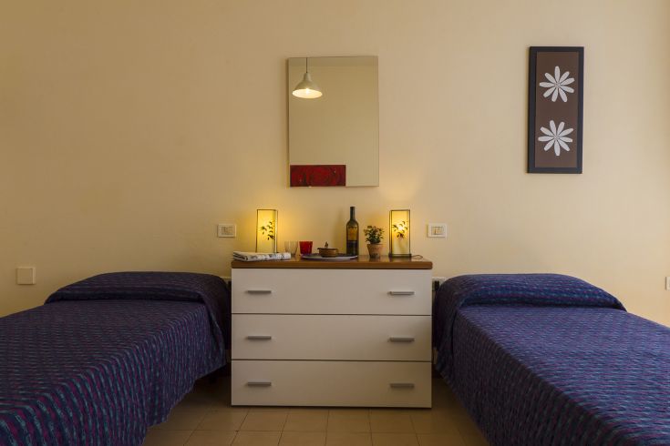 Einfaches Zimmer mit Einzelbetten, schlichter Einrichtung und einigen Blumenarrangements.