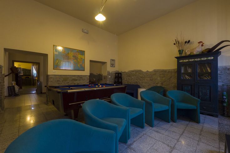 Elegantes Wohnzimmer mit einem Billardtisch und Sesseln. Steinwände und eine gemalte Karte schmücken den Raum.