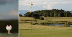 A golf course stretches across a wide green area, featuring a white ball near a yellow flag on the green.