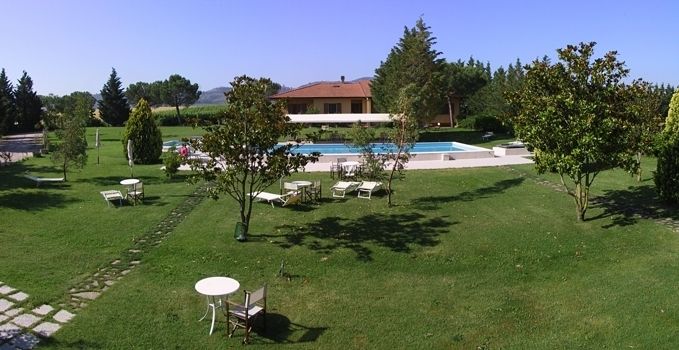 Scene of a mansion with a pool surrounded by trees and green lawns.