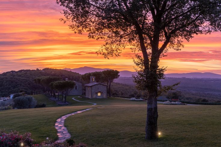 A picturesque sunset landscape in Umbria, featuring gentle hills and a chapel in the background.