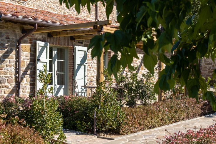 A simple stone facade, surrounded by a well-maintained garden and featuring blue windows.
