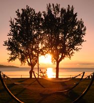 Coucher de soleil sur le lac, avec des arbres et des hamacs créant une atmosphère relaxante.