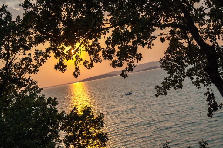 A sunset reflecting on the calm waters of the lake, surrounded by lush green vegetation.