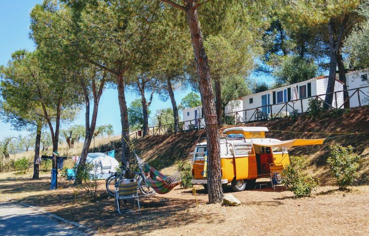 A peaceful camping scene in nature, featuring a yellow van and various camping gear.