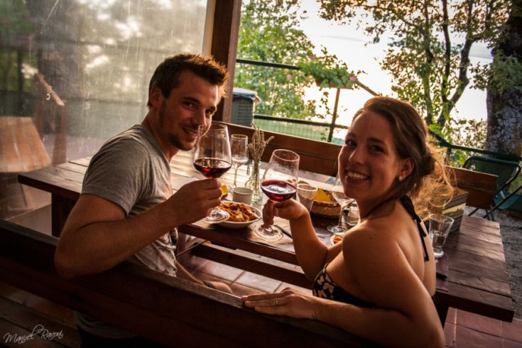 A couple raises glasses of red wine in a serene setting, enjoying a beautiful sunset view.