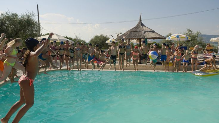 A group of children plays and jumps in the pool, enjoying a sunny summer day.